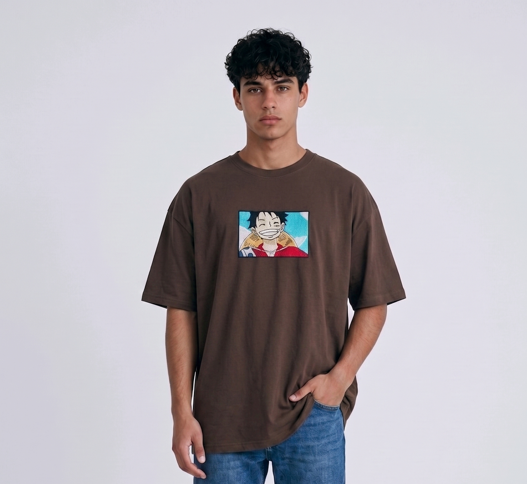 
A full-body studio photograph of a male model wearing an Anetoonz black oversized crewneck t-shirt featuring a framed graphic print of a smiling Monkey D. Luffy with a straw hat against a colorful background.