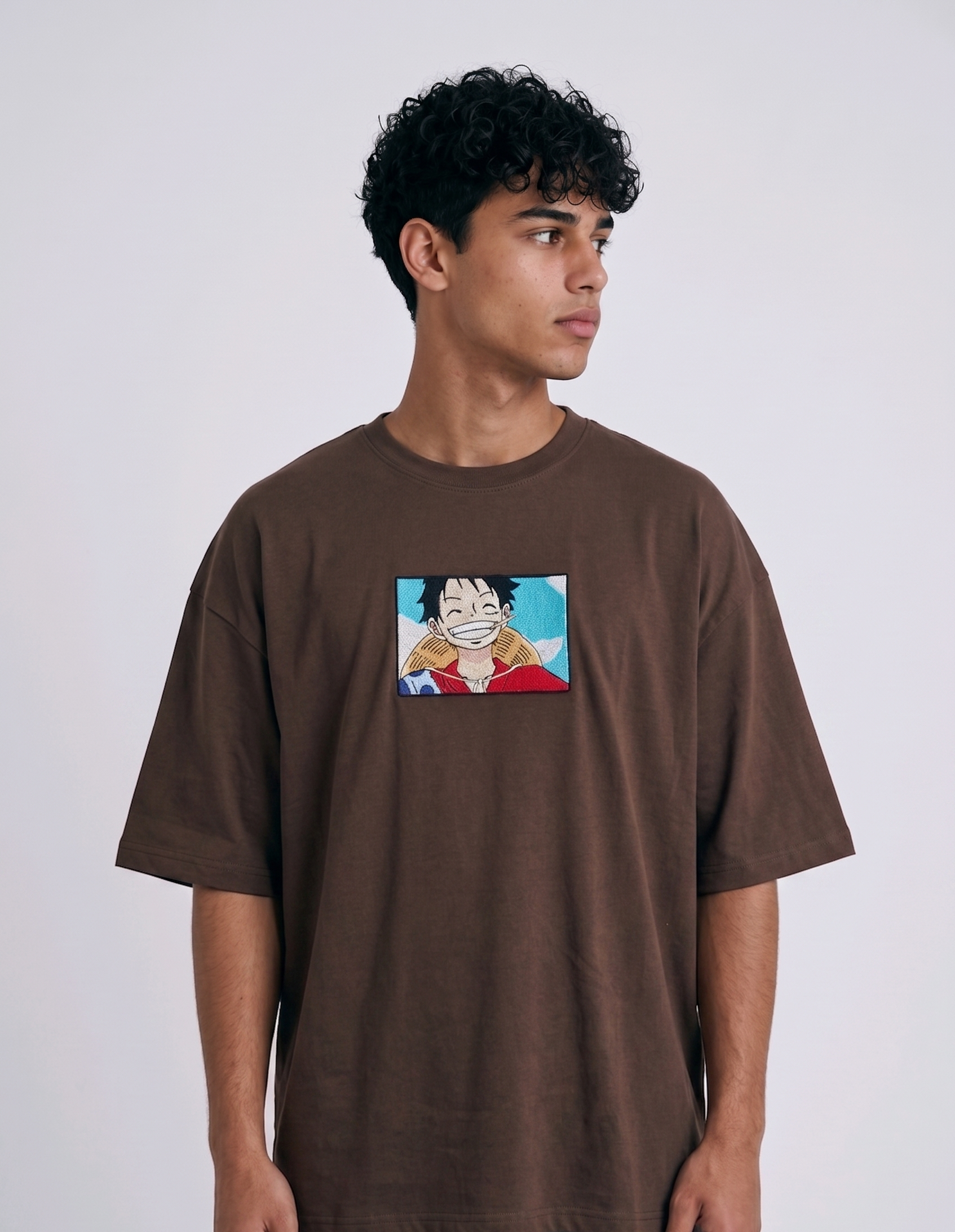 
A full-body studio photograph of a male model wearing an Anetoonz black oversized crewneck t-shirt featuring a framed graphic print of a smiling Monkey D. Luffy with a straw hat against a colorful background.
