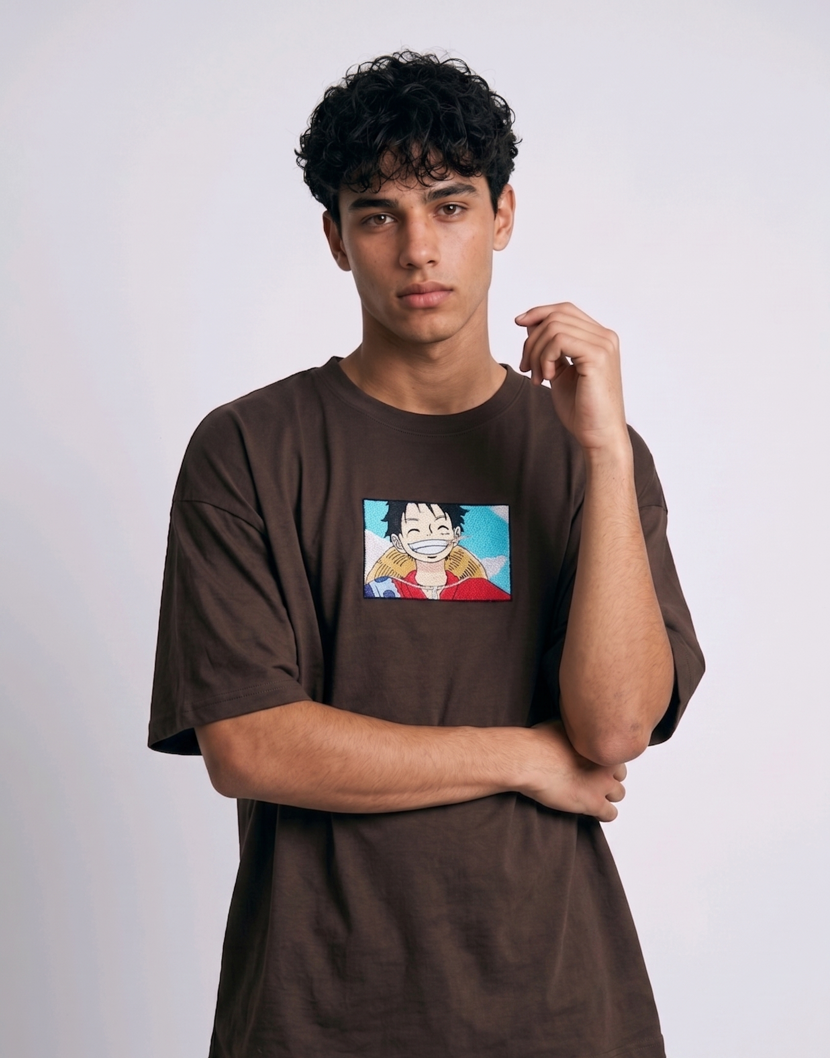 
A full-body studio photograph of a male model wearing an Anetoonz black oversized crewneck t-shirt featuring a framed graphic print of a smiling Monkey D. Luffy with a straw hat against a colorful background.