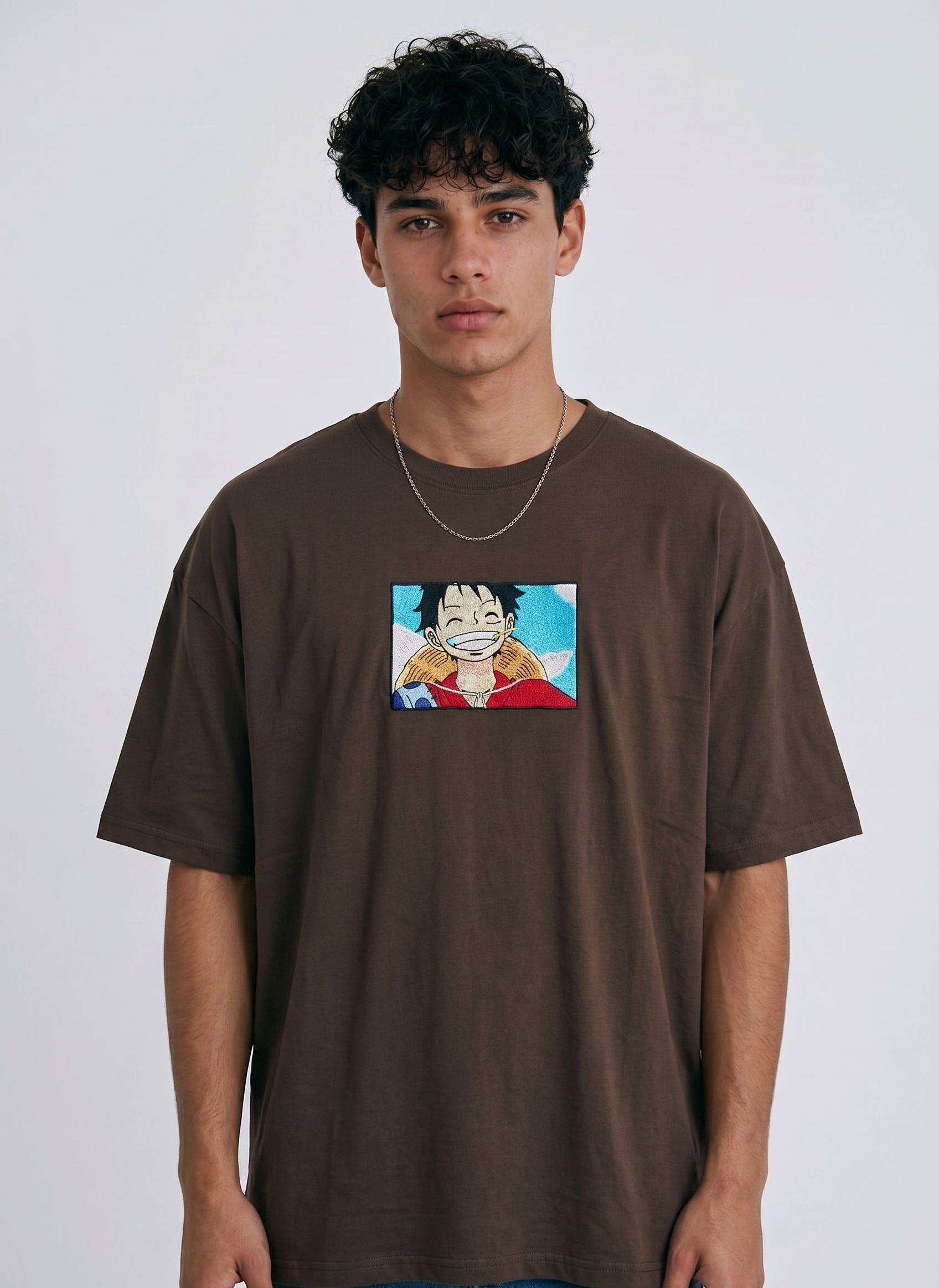 A full-body studio photograph of a male model wearing an Anetoonz black oversized crewneck t-shirt featuring a framed graphic print of a smiling Monkey D. Luffy with a straw hat against a colorful background.