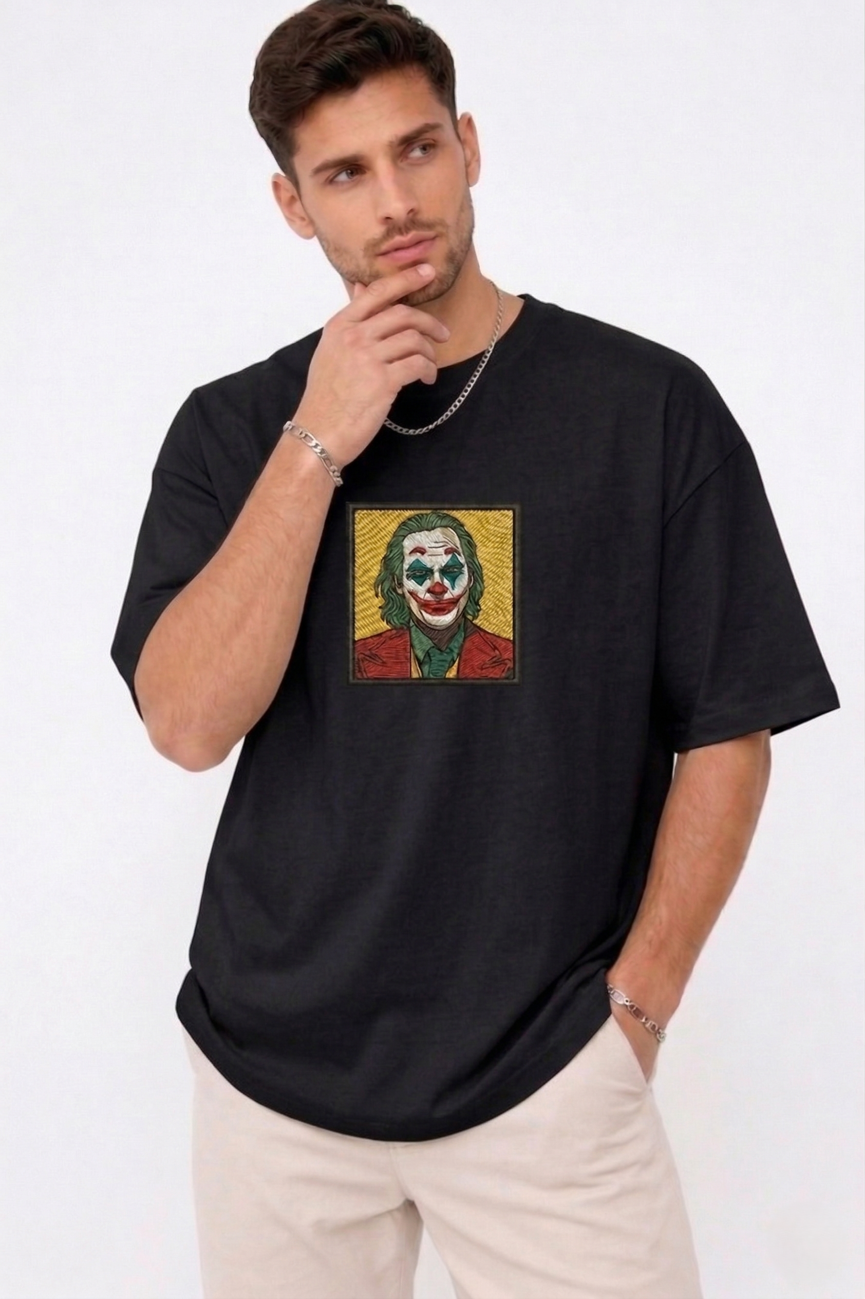 "A man wearing an Anetoonz oversized black half-sleeve T-shirt featuring a square direct embroidery of the Joker character on the chest."