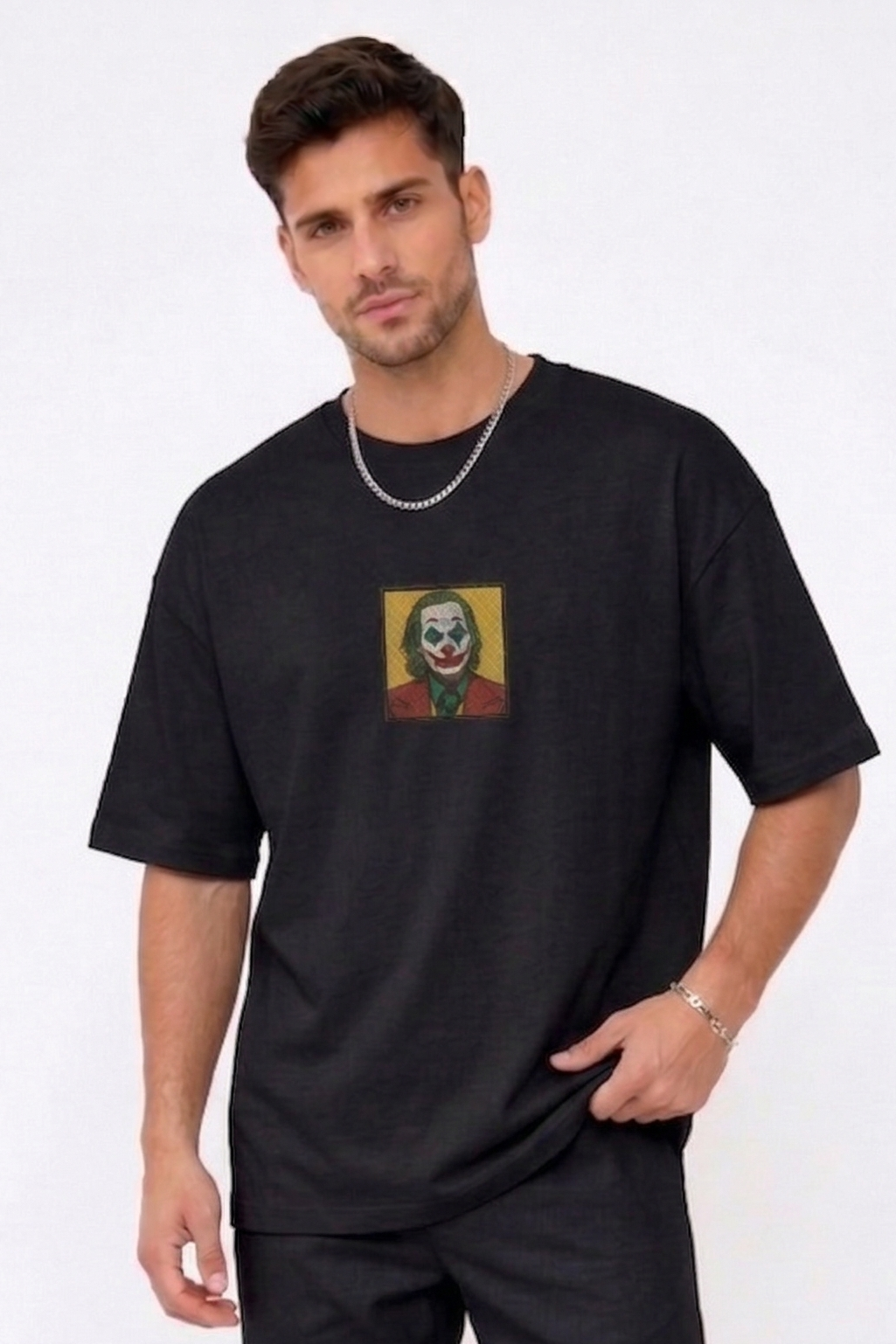 "A man wearing an Anetoonz oversized black half-sleeve T-shirt featuring a square direct embroidery of the Joker character on the chest."