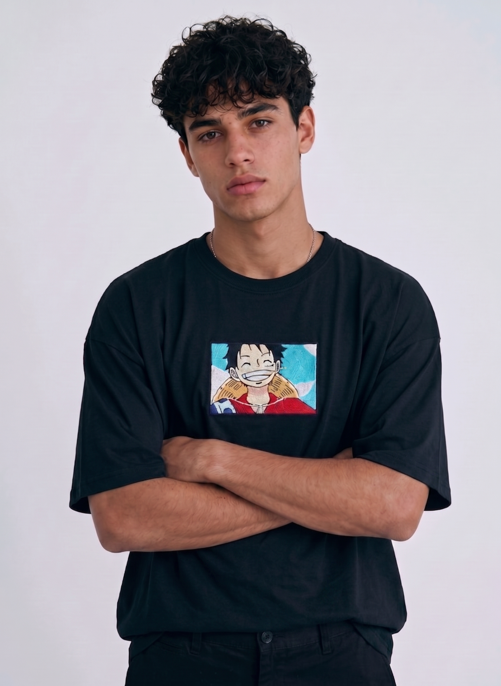 A full-body studio photograph of a male model wearing an Anetoonz black oversized crewneck t-shirt featuring a framed graphic print of a smiling Monkey D. Luffy with a straw hat against a colorful background.