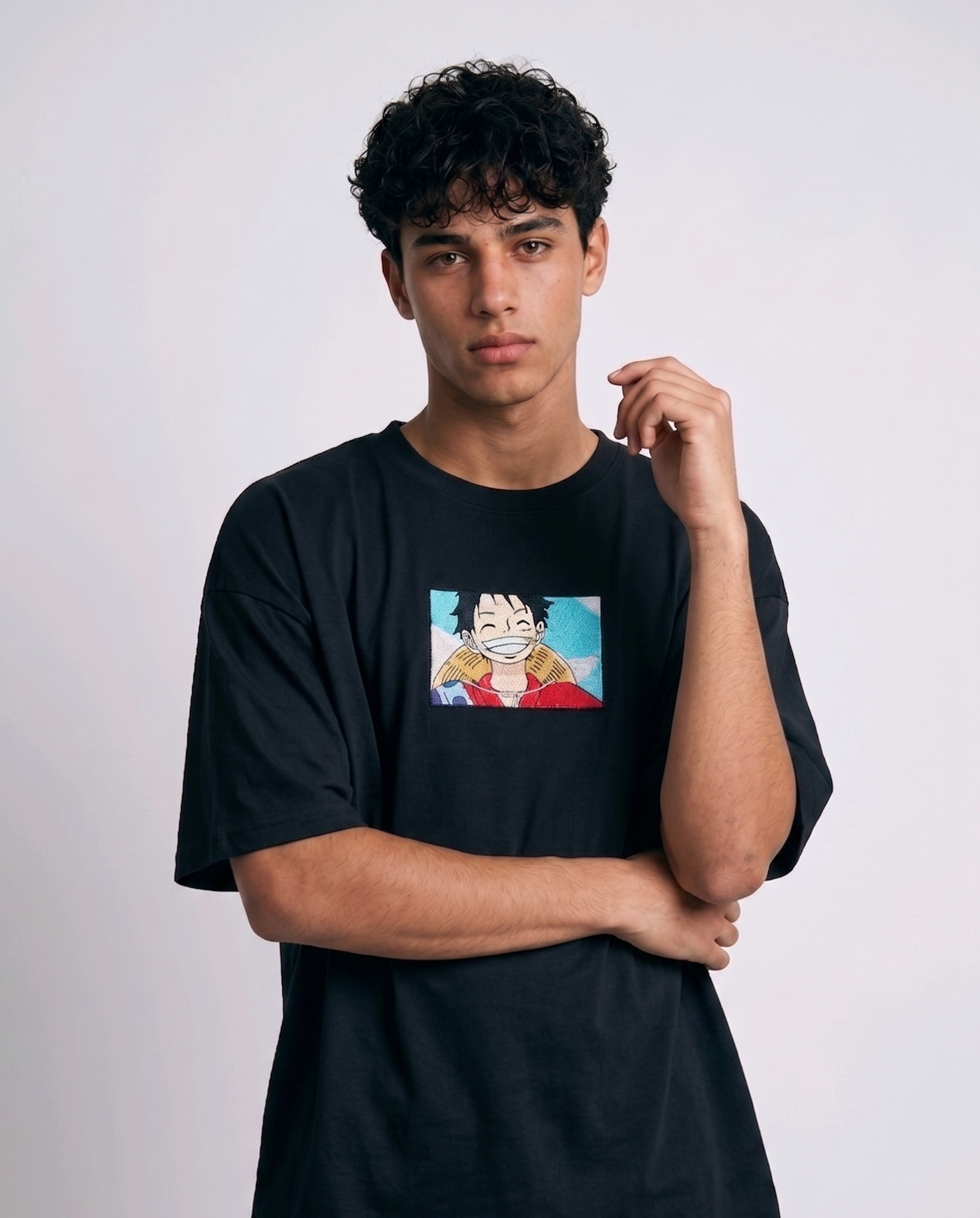 A full-body studio photograph of a male model wearing an Anetoonz black oversized crewneck t-shirt featuring a framed graphic print of a smiling Monkey D. Luffy with a straw hat against a colorful background.