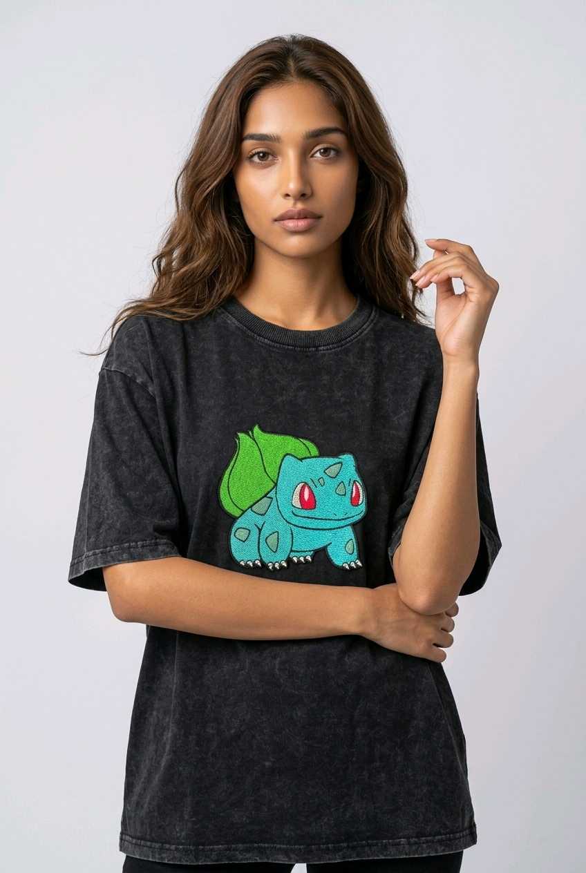 A female model wearing an Acid-Wash oversized t-shirt featuring a detailed green and blue Bulbasaur character embroidered in the center of the chest.
