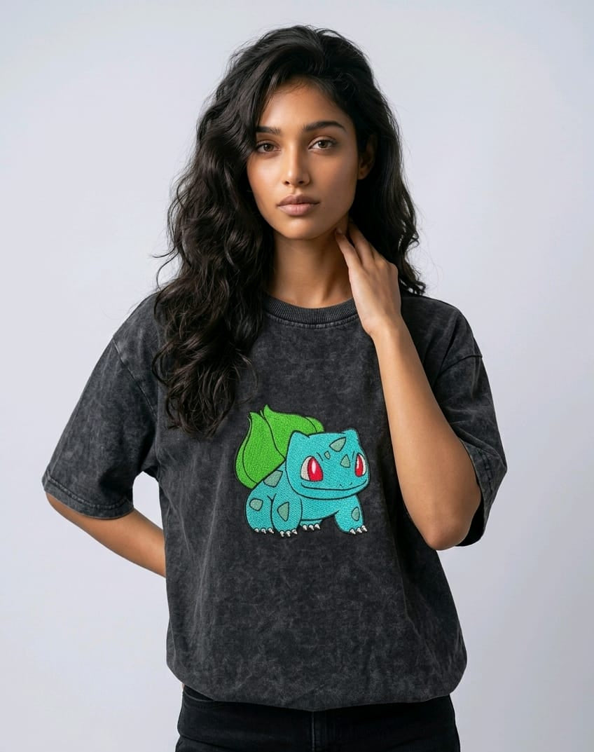 A female model wearing an Acid-Wash oversized t-shirt featuring a detailed green and blue Bulbasaur character embroidered in the center of the chest.