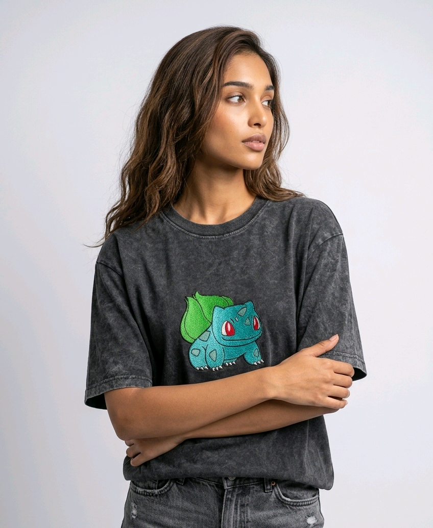 A female model wearing an Acid-Wash oversized t-shirt featuring a detailed green and blue Bulbasaur character embroidered in the center of the chest.