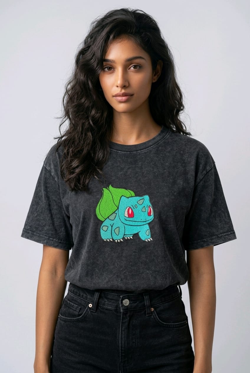 A female model wearing an Acid-Wash oversized t-shirt featuring a detailed green and blue Bulbasaur character embroidered in the center of the chest.