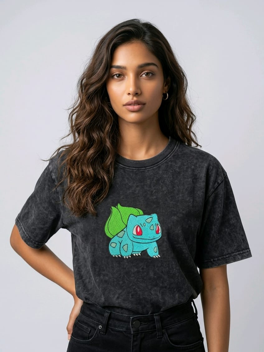A female model wearing an Acid-Wash oversized t-shirt featuring a detailed green and blue Bulbasaur character embroidered in the center of the chest.