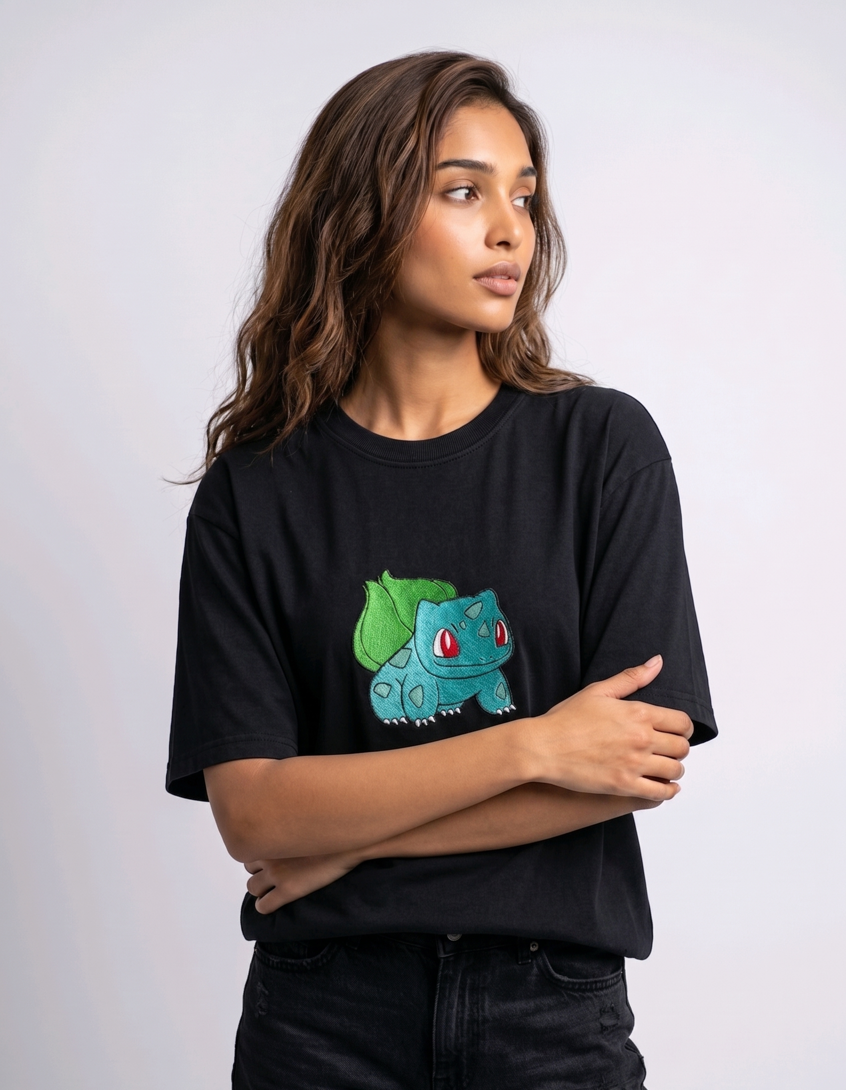 A female model wearing an Black oversized t-shirt featuring a detailed green and blue Bulbasaur character embroidered in the center of the chest.