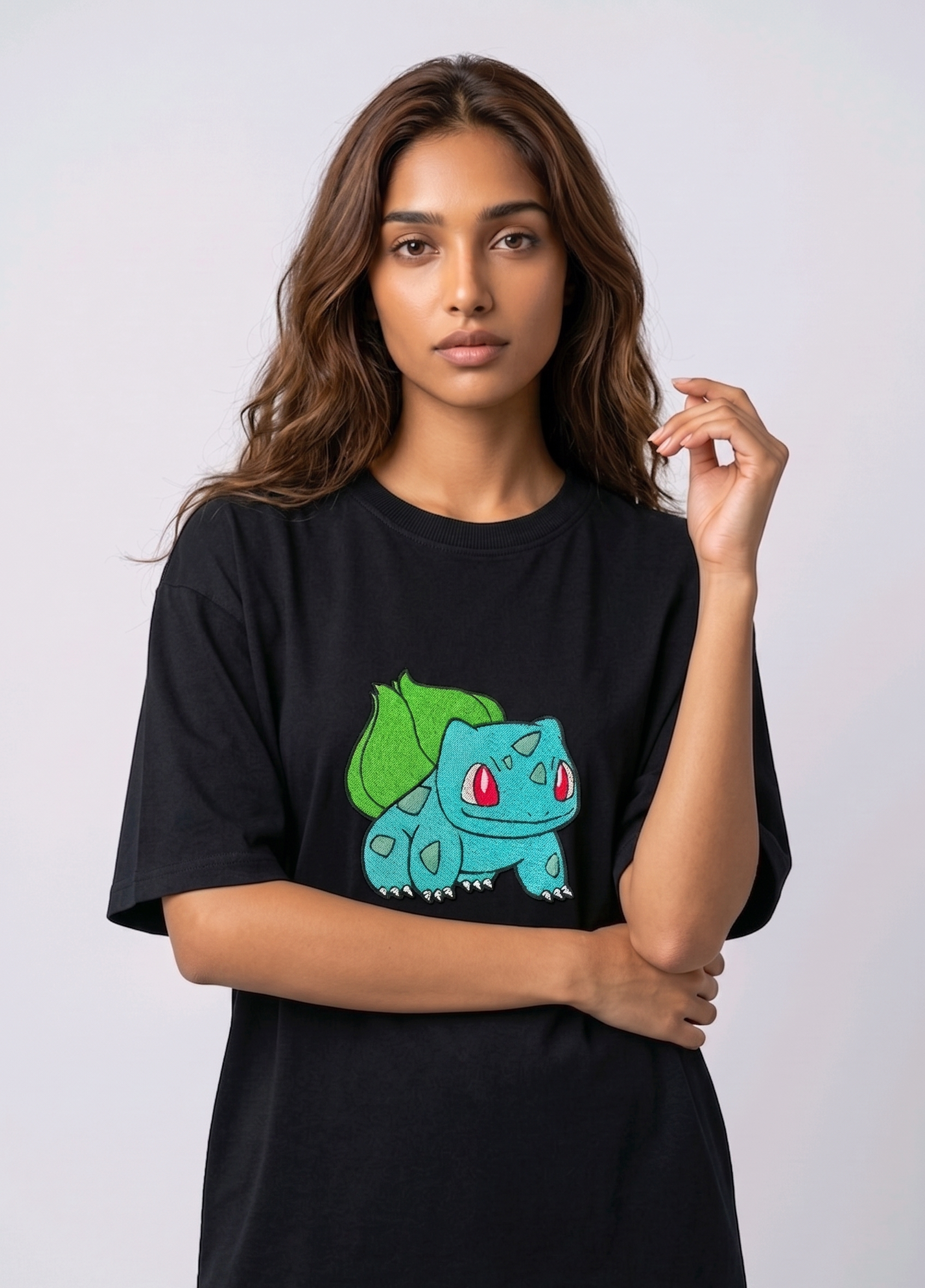 A female model wearing an Black oversized t-shirt featuring a detailed green and blue Bulbasaur character embroidered in the center of the chest.