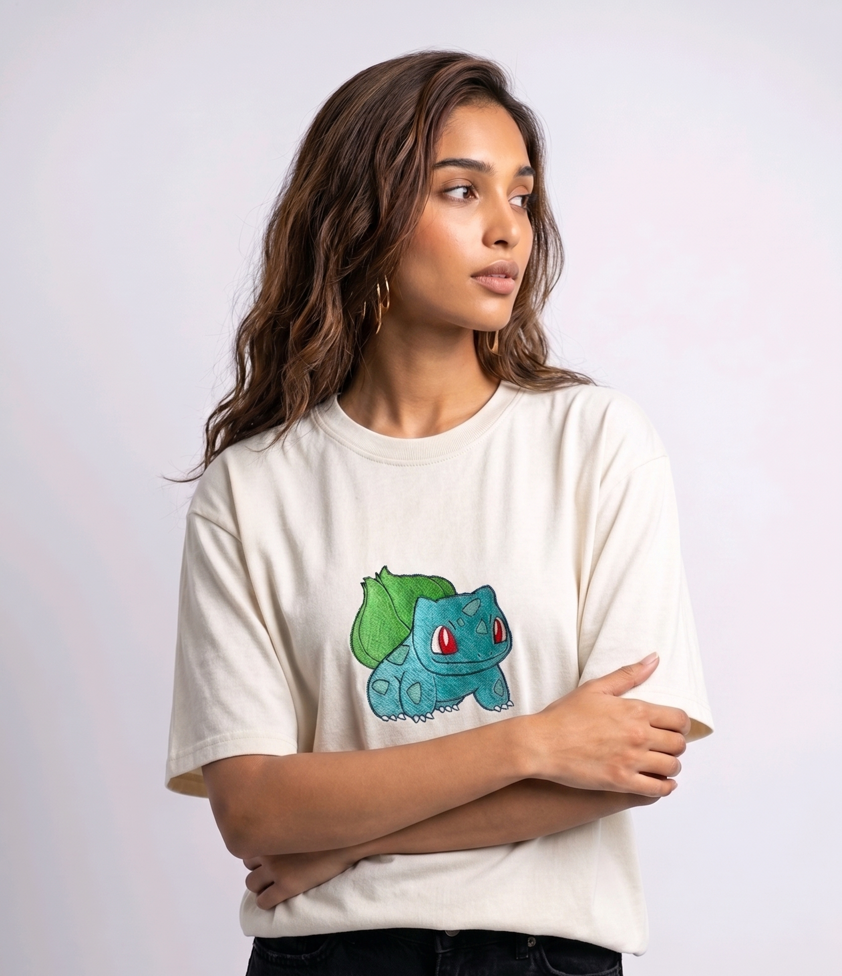 A female model wearing an off-white oversized t-shirt featuring a detailed green and blue Bulbasaur character embroidered in the center of the chest.
