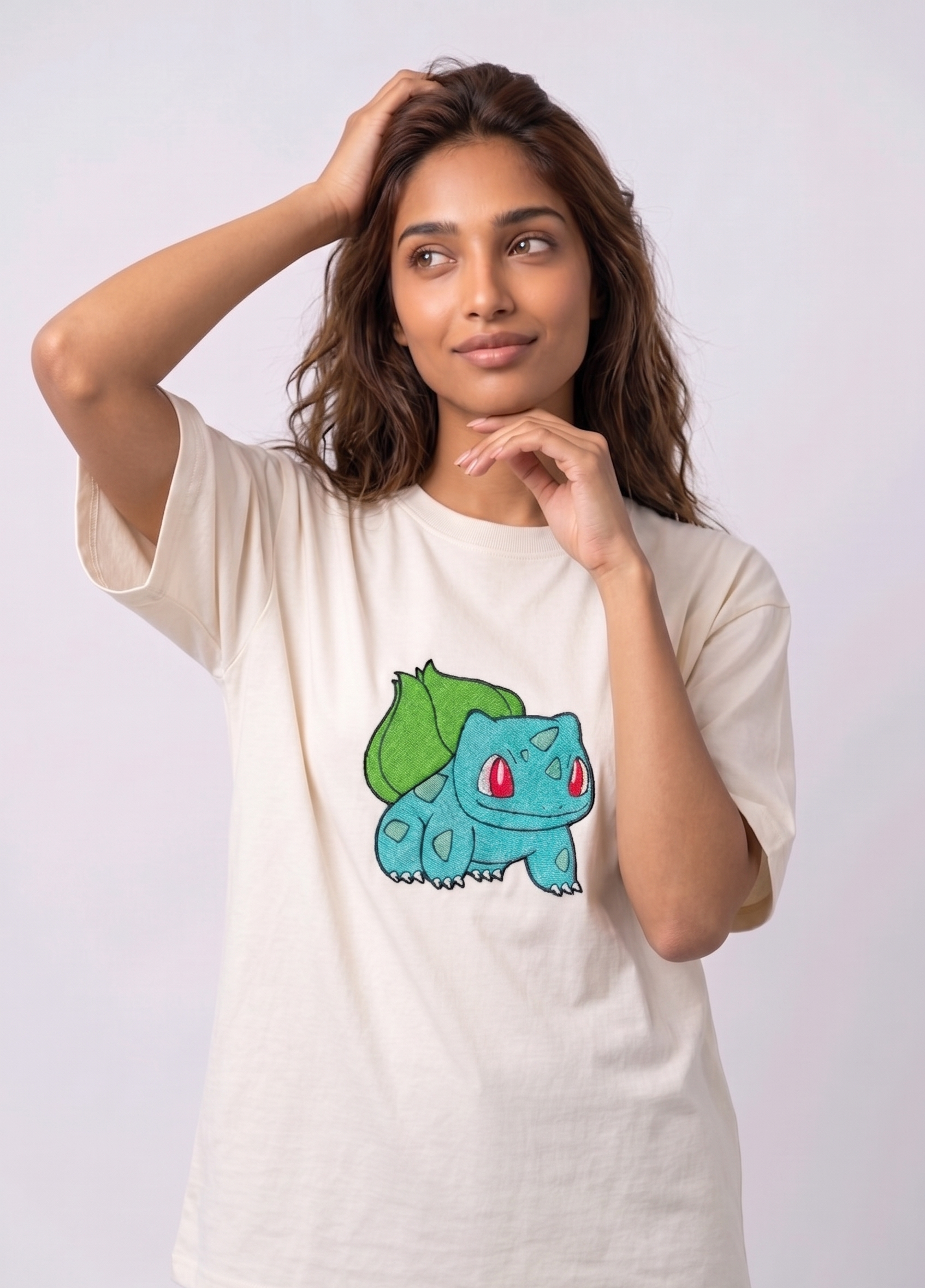 A female model wearing an off-white oversized t-shirt featuring a detailed green and blue Bulbasaur character embroidered in the center of the chest.