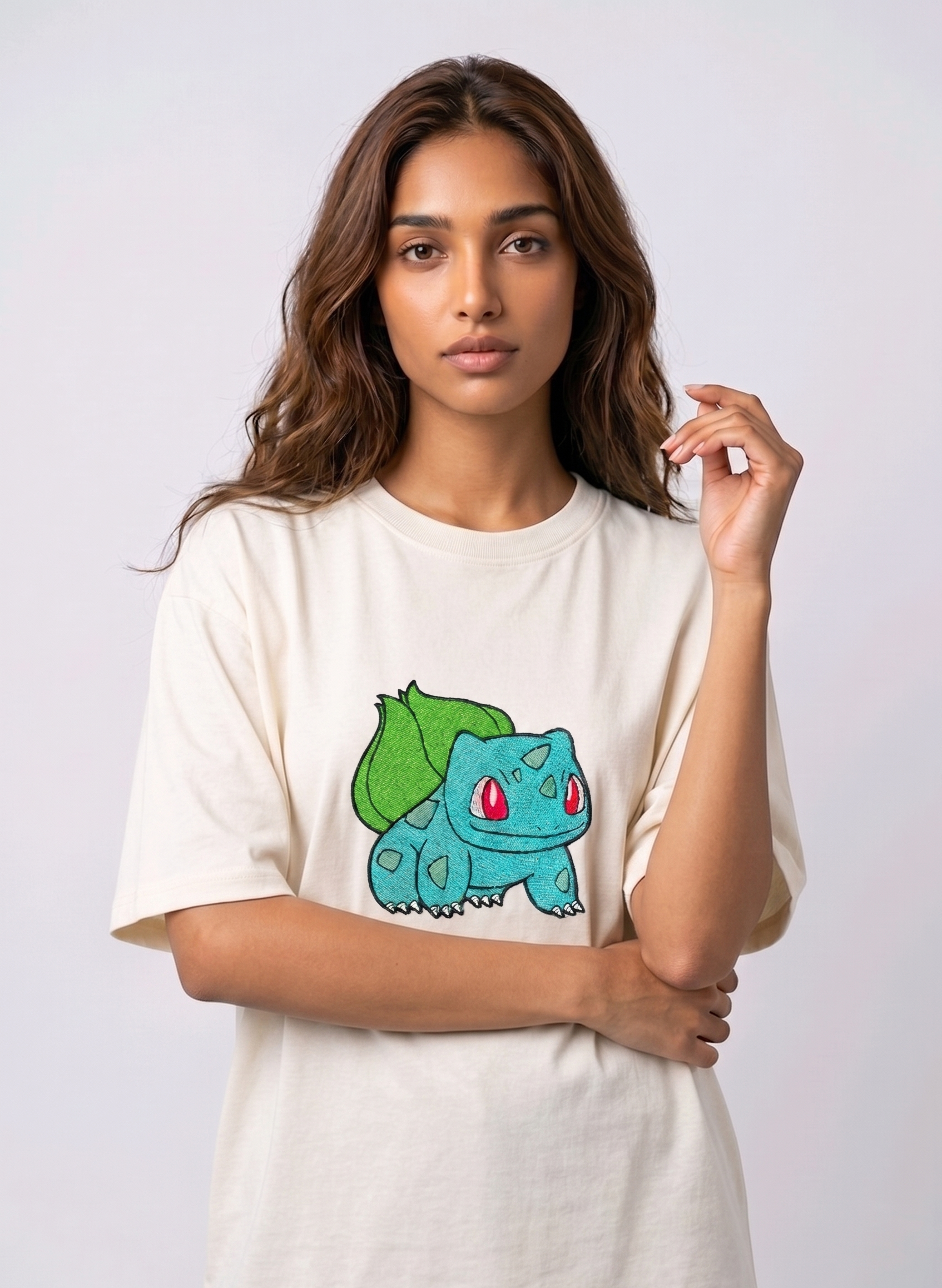 A female model wearing an off-white oversized t-shirt featuring a detailed green and blue Bulbasaur character embroidered in the center of the chest.