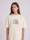 Wearing a cream-colored, crew-neck t-shirt. The center of the chest features a minimalist black line-art embroidery depicting a classic cafe storefront.

