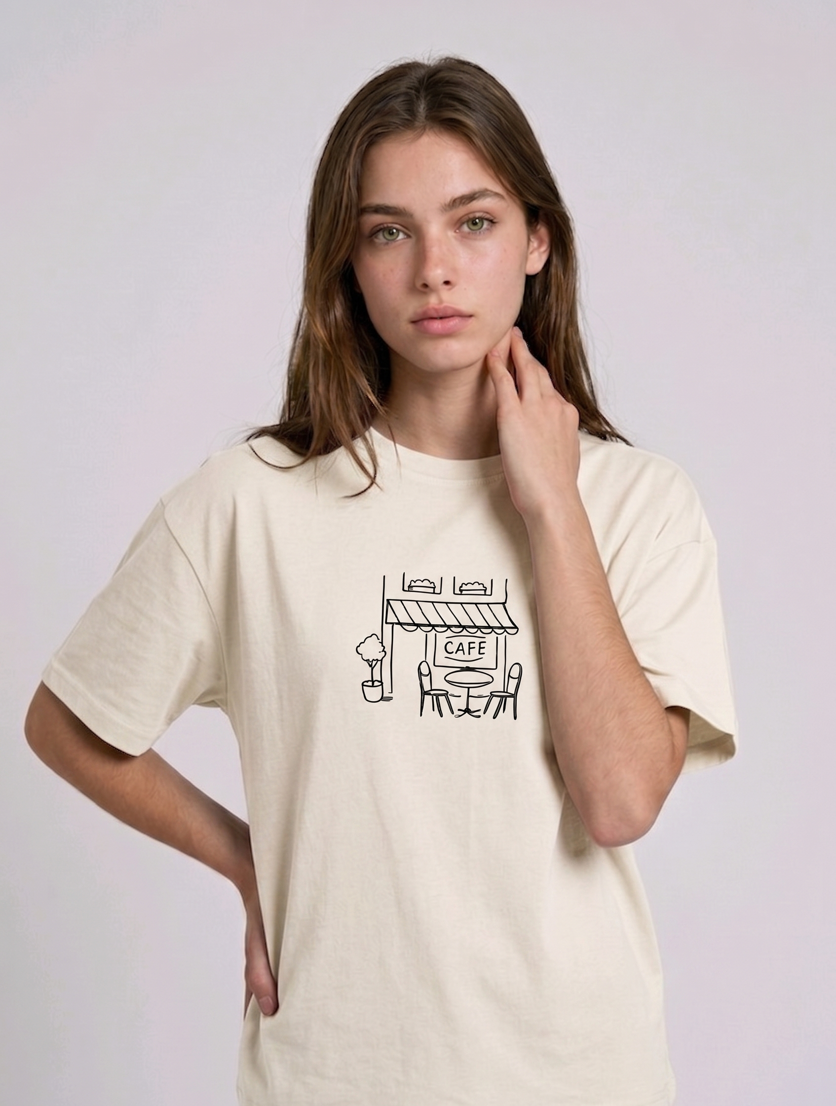 Wearing a cream-colored, crew-neck t-shirt. The center of the chest features a minimalist black line-art embroidery depicting a classic cafe storefront.


