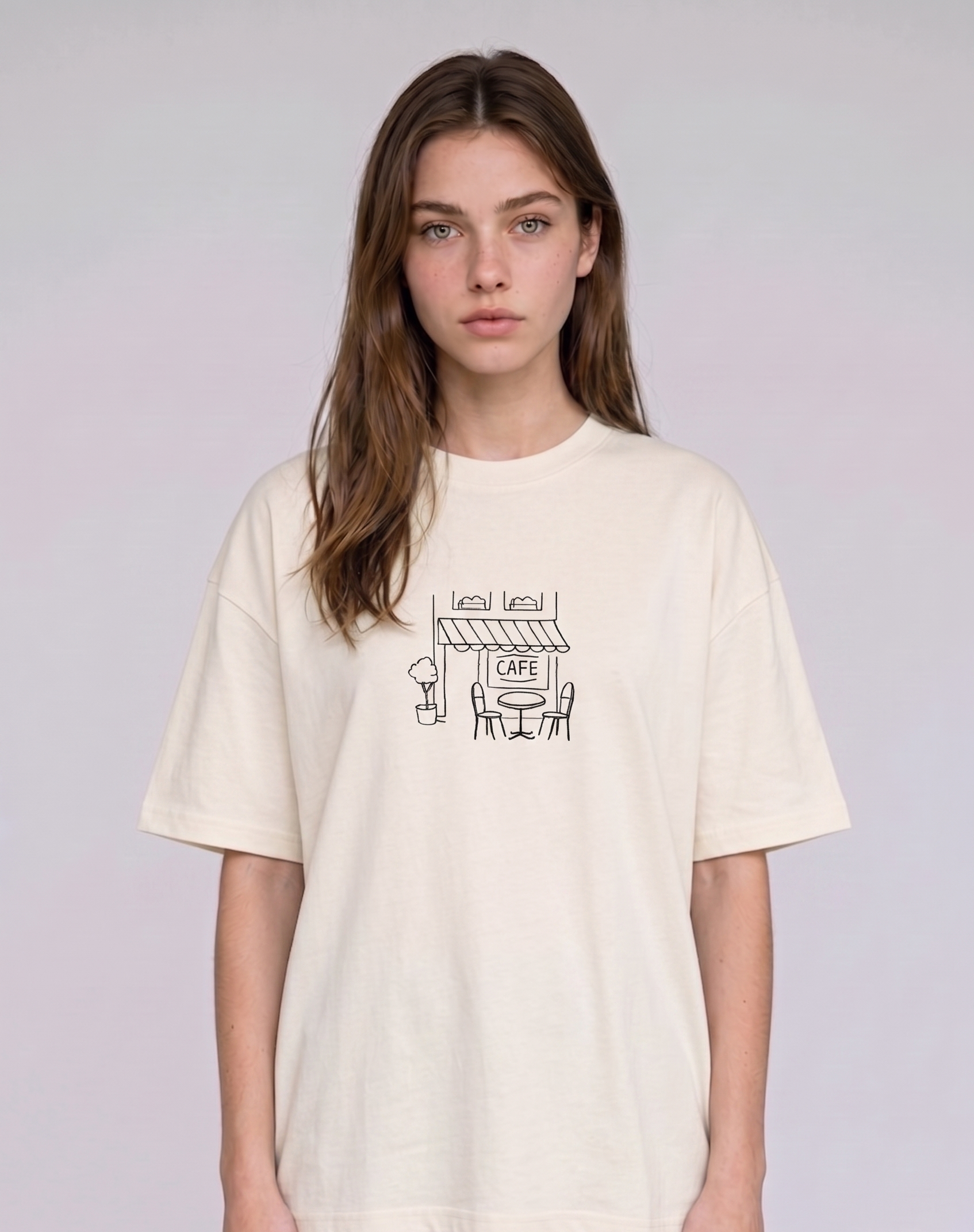 Wearing a cream-colored, crew-neck t-shirt. The center of the chest features a minimalist black line-art embroidery depicting a classic cafe storefront.

