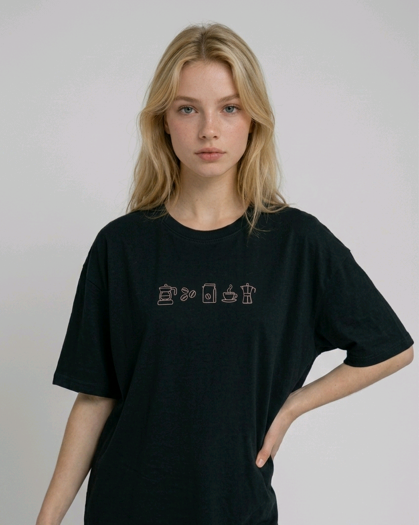 Wearing a cream-colored, crew-neck t-shirt. The center of the chest features a minimalist black line-art embroidery depicting a classic cafe storefront.
