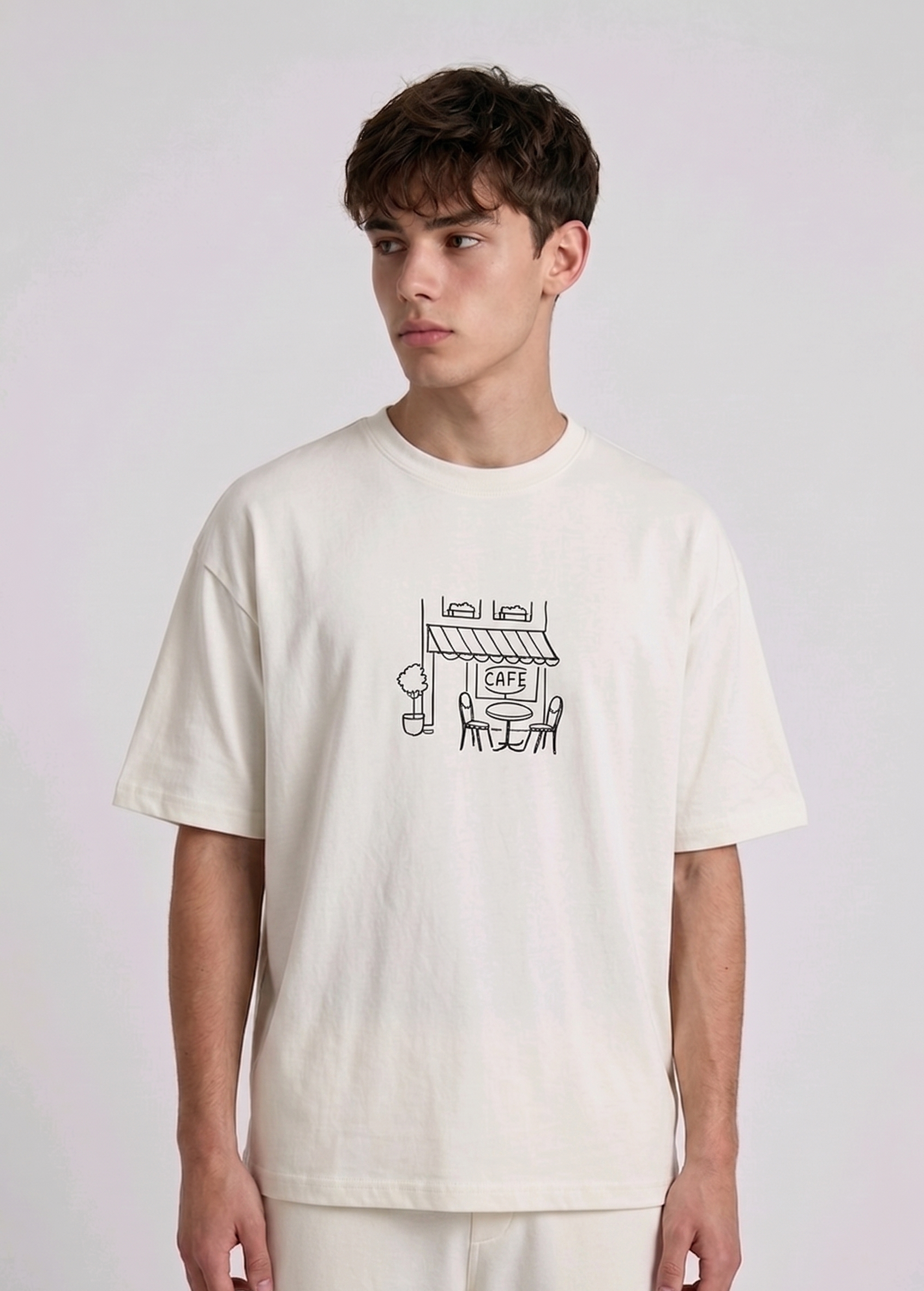 Wearing a cream-colored, crew-neck t-shirt. The center of the chest features a minimalist black line-art embroidery depicting a classic cafe storefront.
