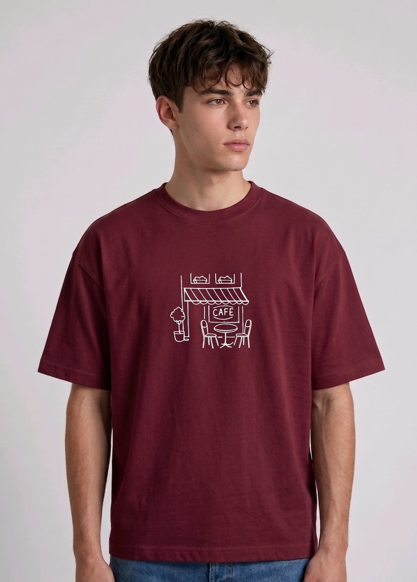Wearing marun-colored, crew-neck t-shirt. The center of the chest features a minimalist white line-art embroidery depicting a classic cafe storefront.
