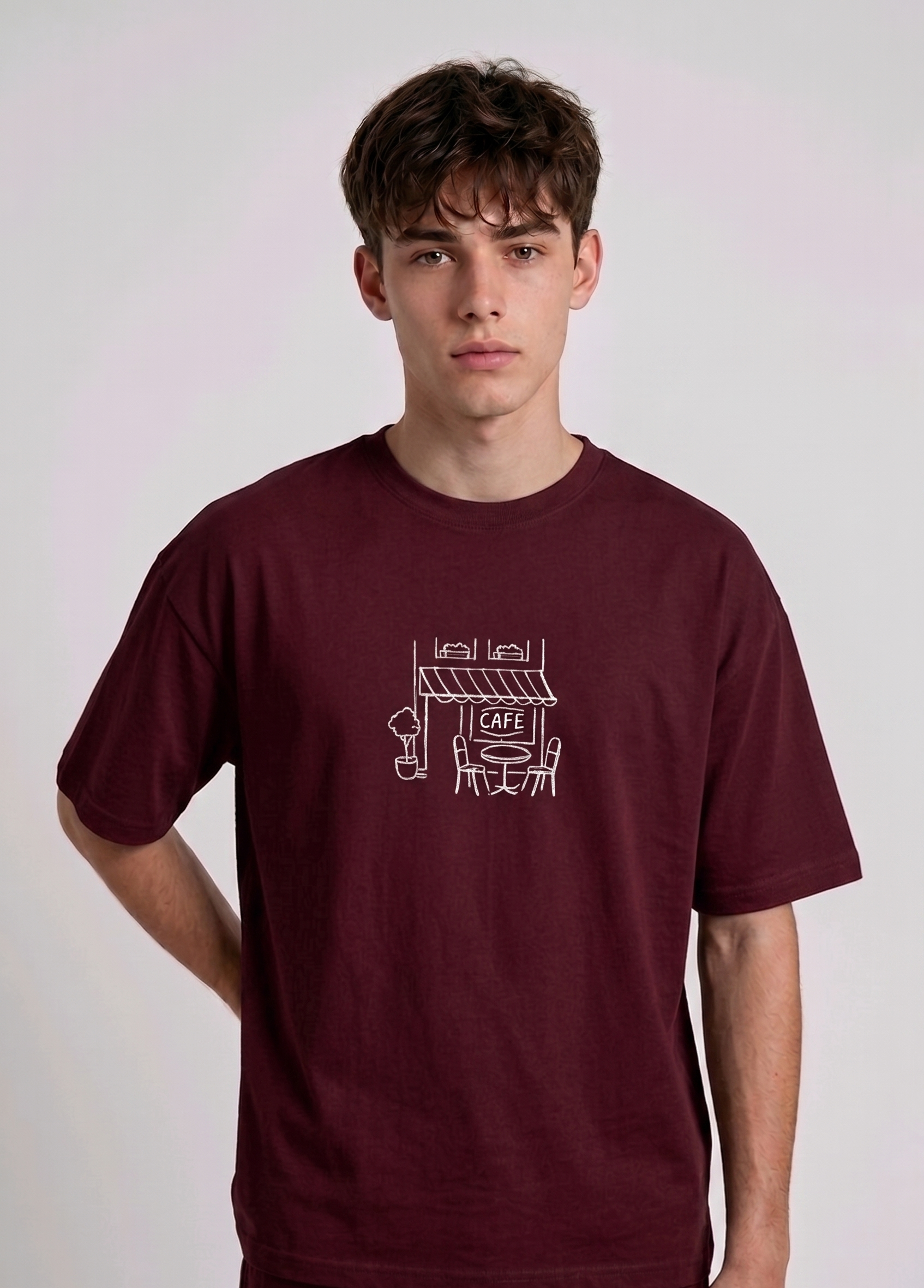 Wearing marun-colored, crew-neck t-shirt. The center of the chest features a minimalist white line-art embroidery depicting a classic cafe storefront.