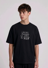 Wearing Black-colored, crew-neck t-shirt. The center of the chest features a minimalist white line-art embroidery depicting a classic cafe storefront.
