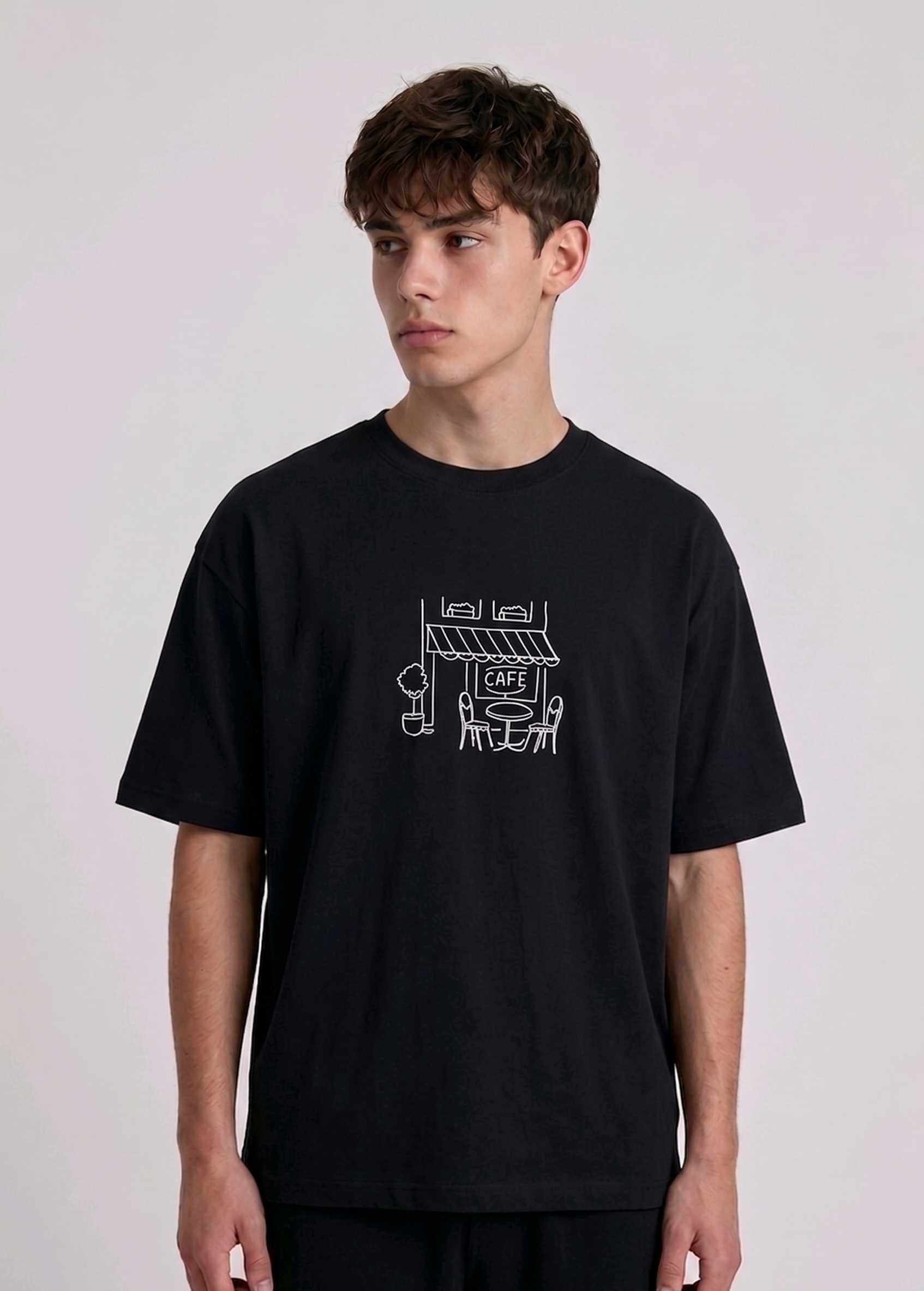 Wearing Black-colored, crew-neck t-shirt. The center of the chest features a minimalist white line-art embroidery depicting a classic cafe storefront.
