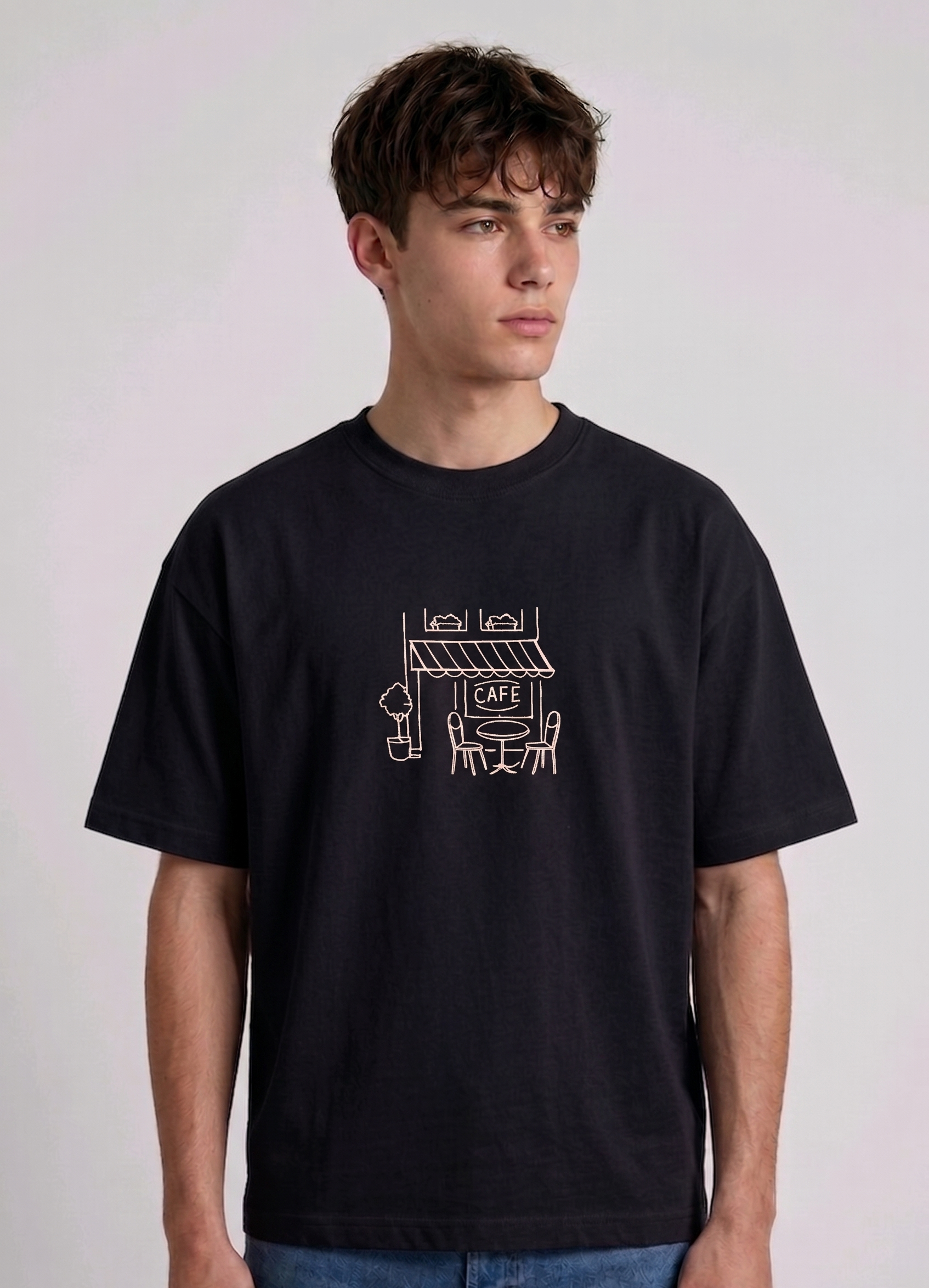 Wearing Black-colored, crew-neck t-shirt. The center of the chest features a minimalist white line-art embroidery depicting a classic cafe storefront.
