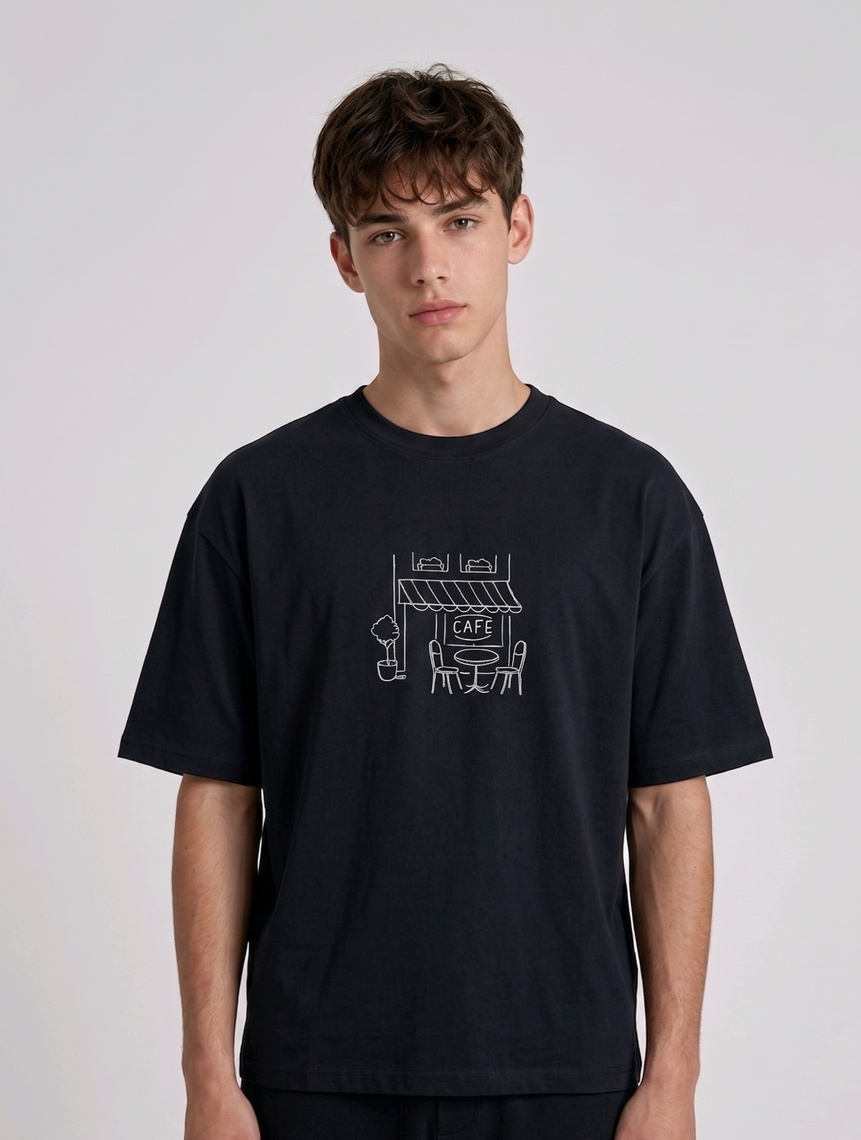 Wearing Black-colored, crew-neck t-shirt. The center of the chest features a minimalist white line-art embroidery depicting a classic cafe storefront.
