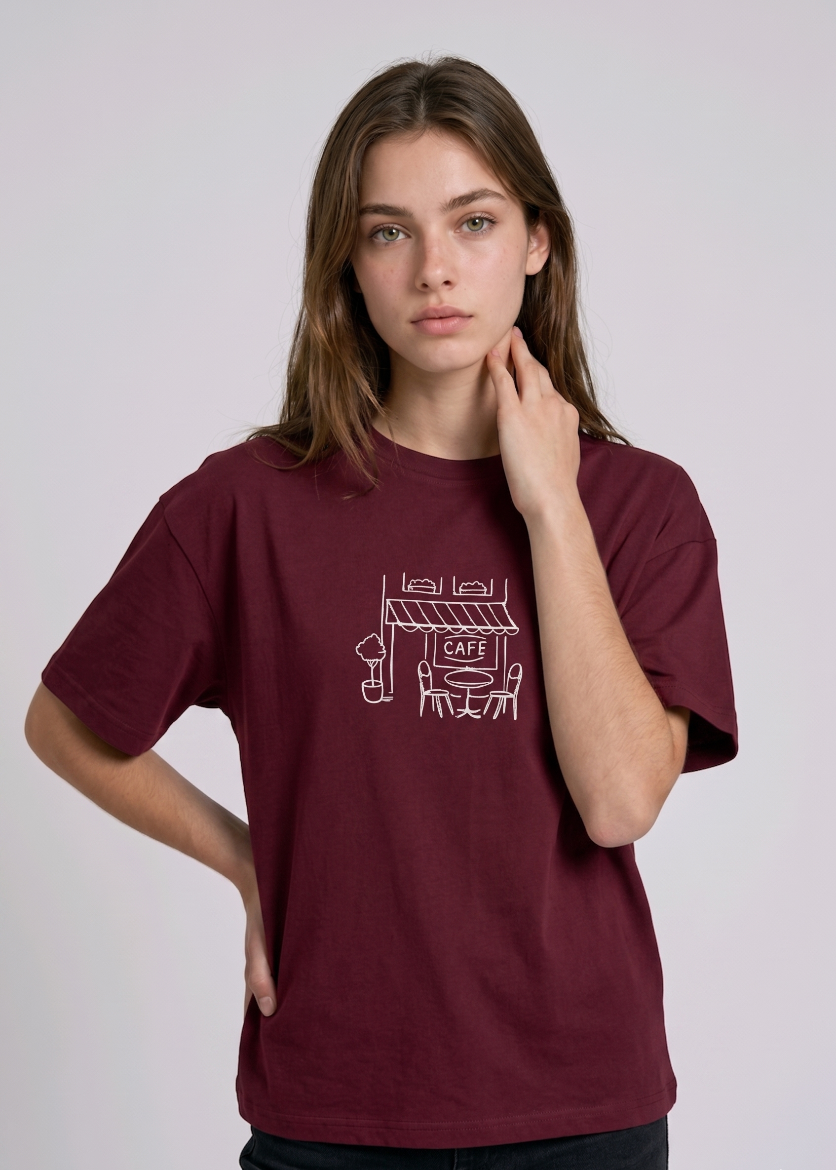Wearing a cream-colored, crew-neck t-shirt. The center of the chest features a minimalist black line-art embroidery depicting a classic cafe storefront.

