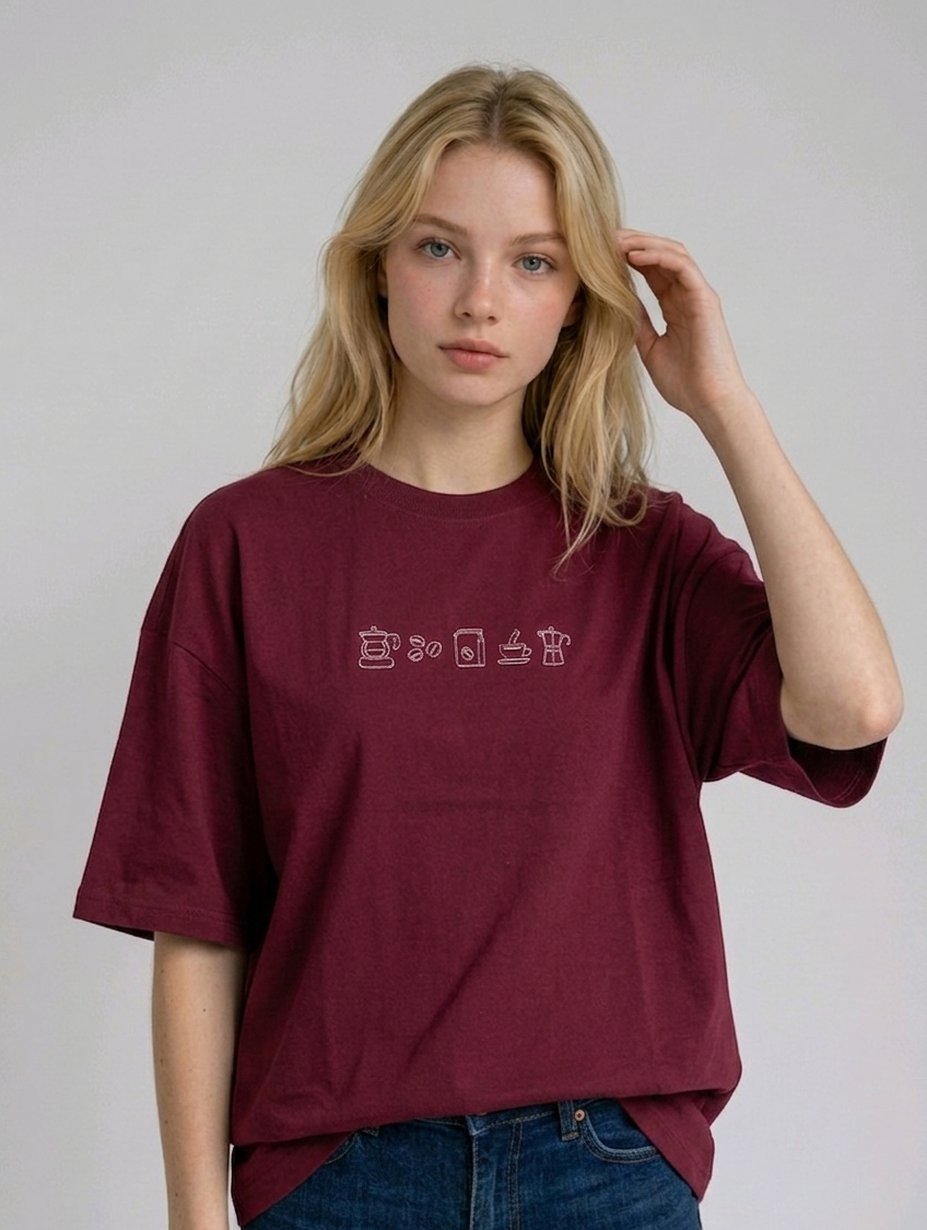 wearing an oversized, half-sleeved heavyweight cotton t-shirt. The chest features high-density direct embroidery of five minimalist coffee-themed icons in a horizontal row, including a French press, coffee beans, a coffee bag, a steaming cup, and a moka pot.
