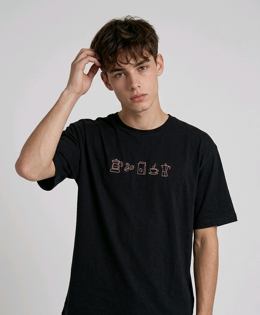 wearing an oversized, half-sleeved heavyweight cotton t-shirt. The chest features high-density direct embroidery of five minimalist coffee-themed icons in a horizontal row, including a French press, coffee beans, a coffee bag, a steaming cup, and a moka pot.
