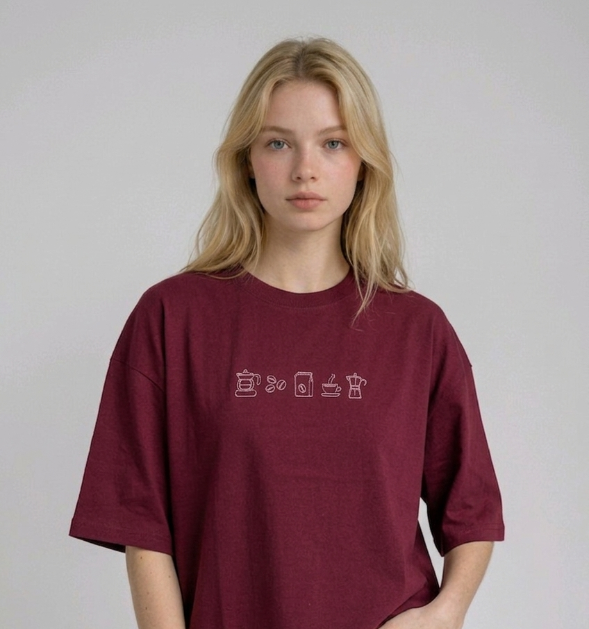 wearing an oversized, half-sleeved heavyweight cotton t-shirt. The chest features high-density direct embroidery of five minimalist coffee-themed icons in a horizontal row, including a French press, coffee beans, a coffee bag, a steaming cup, and a moka pot.
