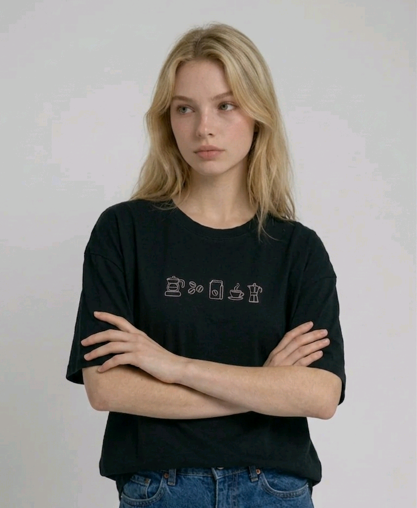 wearing an oversized, half-sleeved heavyweight cotton t-shirt. The chest features high-density direct embroidery of five minimalist coffee-themed icons in a horizontal row, including a French press, coffee beans, a coffee bag, a steaming cup, and a moka pot.
