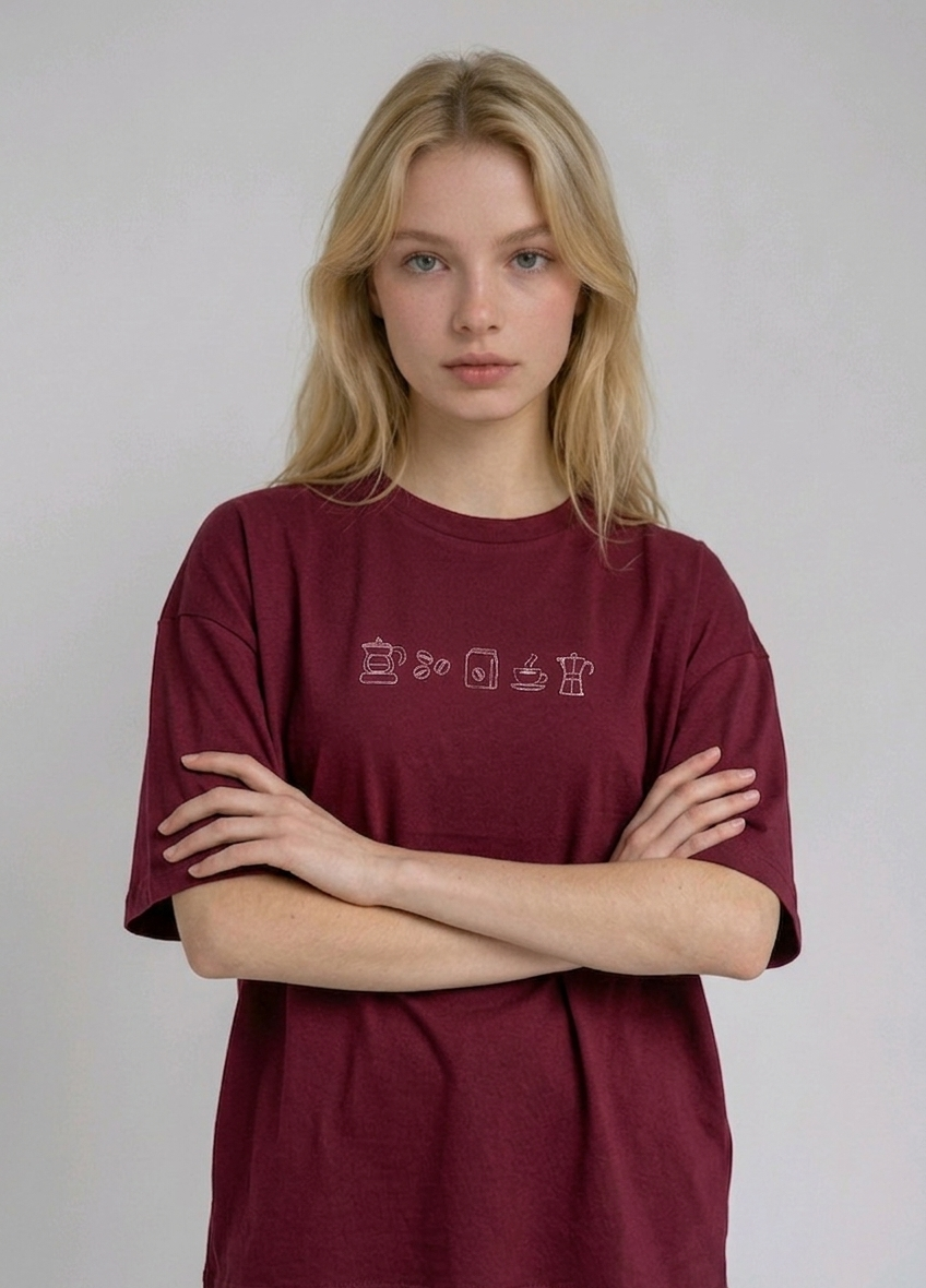wearing an oversized, half-sleeved heavyweight cotton t-shirt. The chest features high-density direct embroidery of five minimalist coffee-themed icons in a horizontal row, including a French press, coffee beans, a coffee bag, a steaming cup, and a moka pot.
