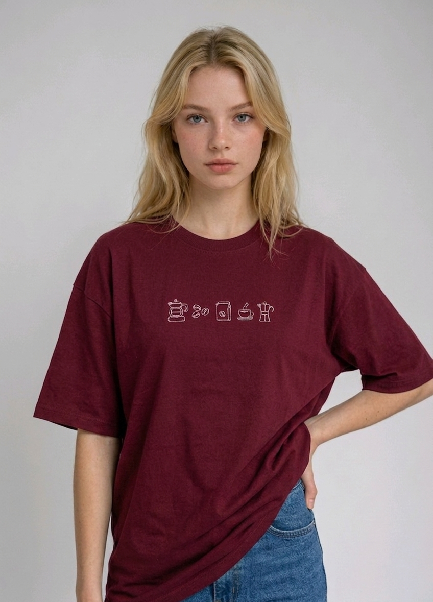 wearing an oversized, half-sleeved heavyweight cotton t-shirt. The chest features high-density direct embroidery of five minimalist coffee-themed icons in a horizontal row, including a French press, coffee beans, a coffee bag, a steaming cup, and a moka pot.
