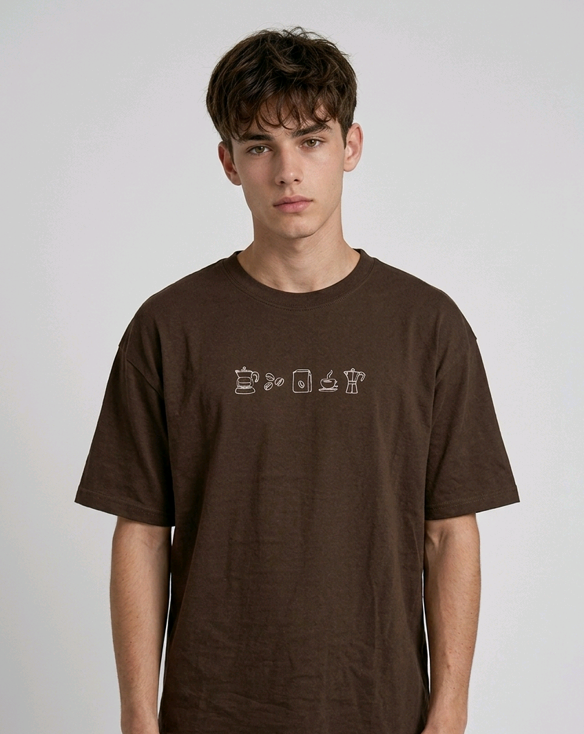 wearing an oversized, half-sleeved heavyweight cotton t-shirt. The chest features high-density direct embroidery of five minimalist coffee-themed icons in a horizontal row, including a French press, coffee beans, a coffee bag, a steaming cup, and a moka pot.
