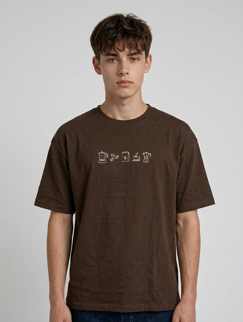 wearing an oversized, half-sleeved heavyweight cotton t-shirt. The chest features high-density direct embroidery of five minimalist coffee-themed icons in a horizontal row, including a French press, coffee beans, a coffee bag, a steaming cup, and a moka pot.
