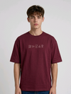 wearing an oversized, half-sleeved heavyweight cotton t-shirt. The chest features high-density direct embroidery of five minimalist coffee-themed icons in a horizontal row, including a French press, coffee beans, a coffee bag, a steaming cup, and a moka pot.
