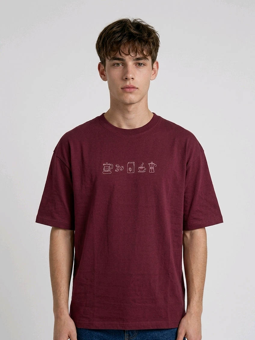 wearing an oversized, half-sleeved heavyweight cotton t-shirt. The chest features high-density direct embroidery of five minimalist coffee-themed icons in a horizontal row, including a French press, coffee beans, a coffee bag, a steaming cup, and a moka pot.
