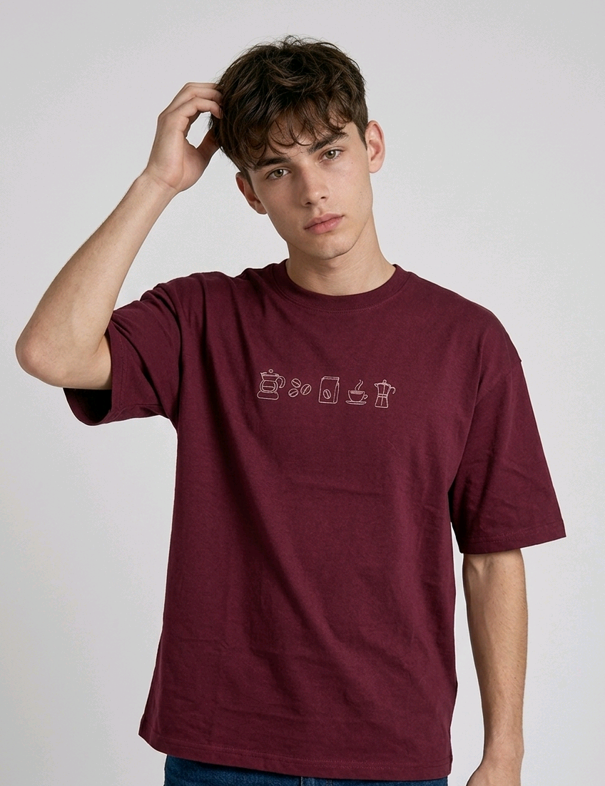wearing an oversized, half-sleeved heavyweight cotton t-shirt. The chest features high-density direct embroidery of five minimalist coffee-themed icons in a horizontal row, including a French press, coffee beans, a coffee bag, a steaming cup, and a moka pot.
