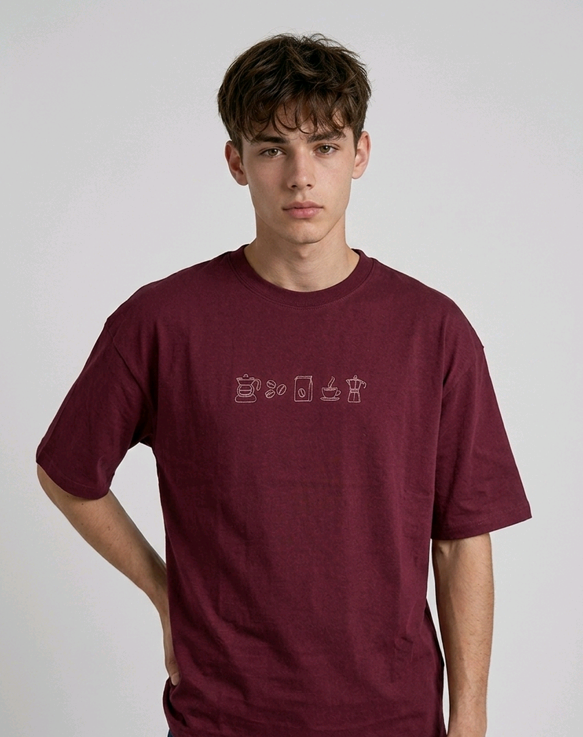 wearing an oversized, half-sleeved heavyweight cotton t-shirt. The chest features high-density direct embroidery of five minimalist coffee-themed icons in a horizontal row, including a French press, coffee beans, a coffee bag, a steaming cup, and a moka pot.
