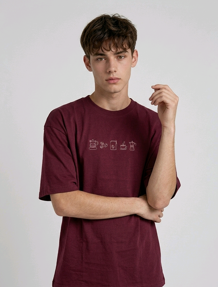 wearing an oversized, half-sleeved heavyweight cotton t-shirt. The chest features high-density direct embroidery of five minimalist coffee-themed icons in a horizontal row, including a French press, coffee beans, a coffee bag, a steaming cup, and a moka pot.
