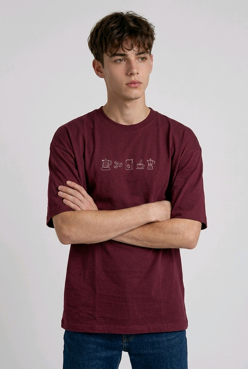wearing an oversized, half-sleeved heavyweight cotton t-shirt. The chest features high-density direct embroidery of five minimalist coffee-themed icons in a horizontal row, including a French press, coffee beans, a coffee bag, a steaming cup, and a moka pot.
