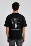 A male model from the back, wearing a black oversized t-shirt with a large, detailed embroidery design.
