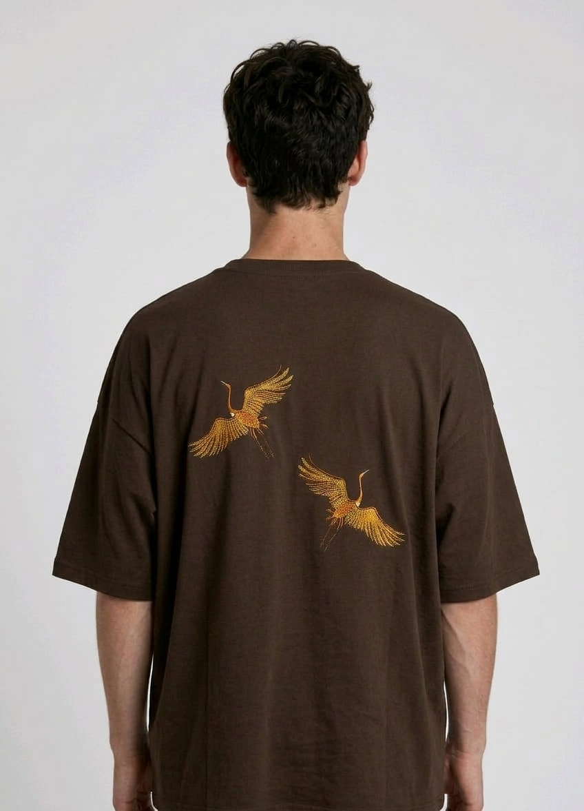 Rear view of a person wearing a heavyweight oversized half-sleeved t-shirt featuring high-density direct embroidery of two golden cranes on the back.

