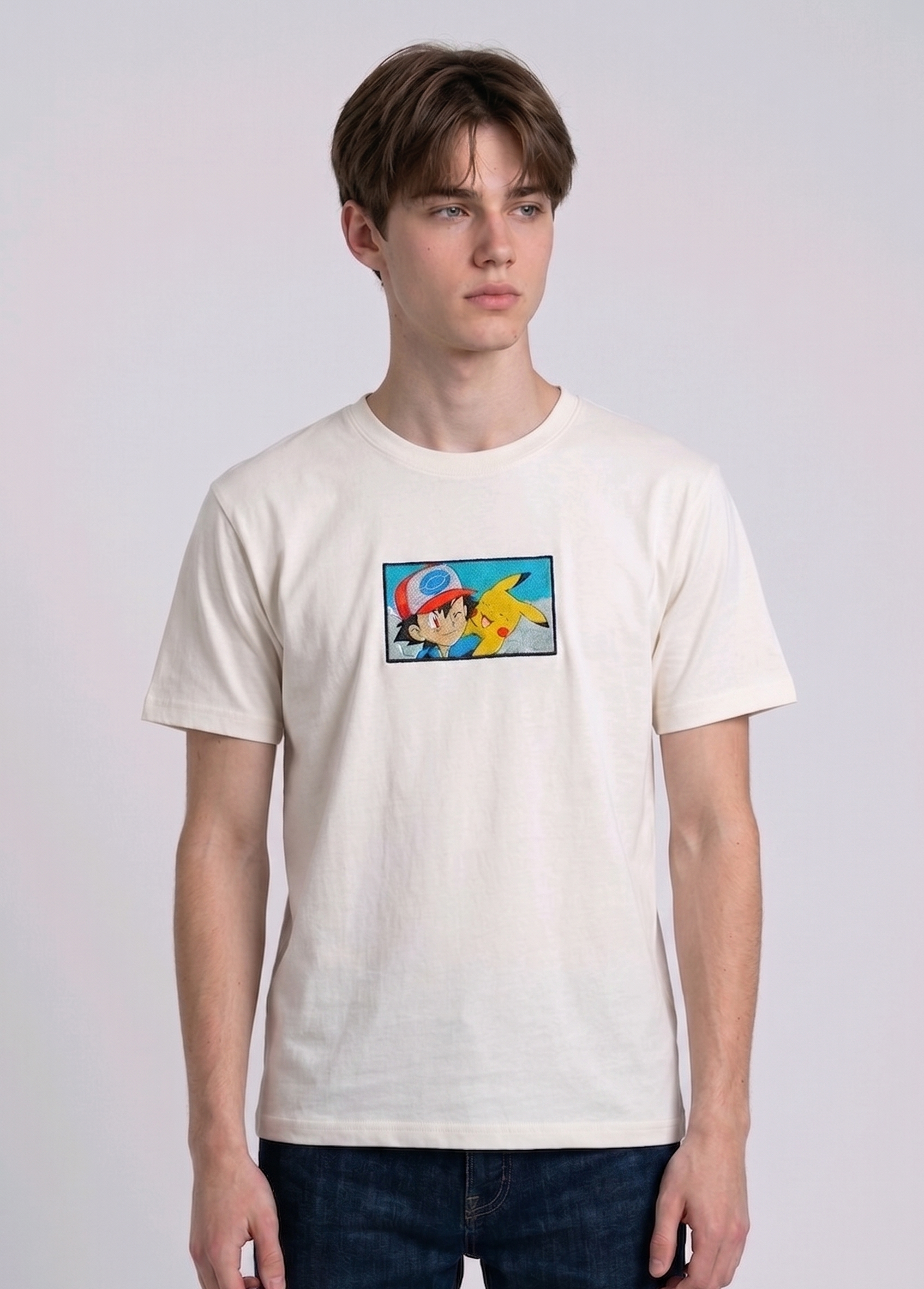 He is wearing heavyweight cotton t-shirt with a detailed, colorful embroidered patch on the chest featuring anime characters Ash Ketchum (winking) and Pikachu.