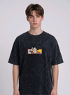 Front view of a male model with middle-parted brown hair wearing an Anetoonz dark grey mineral wash oversized t-shirt featuring a detailed, embroidered graphic of Son Goku from Dragon Ball Z giving a peace sign within a colorful framed background.