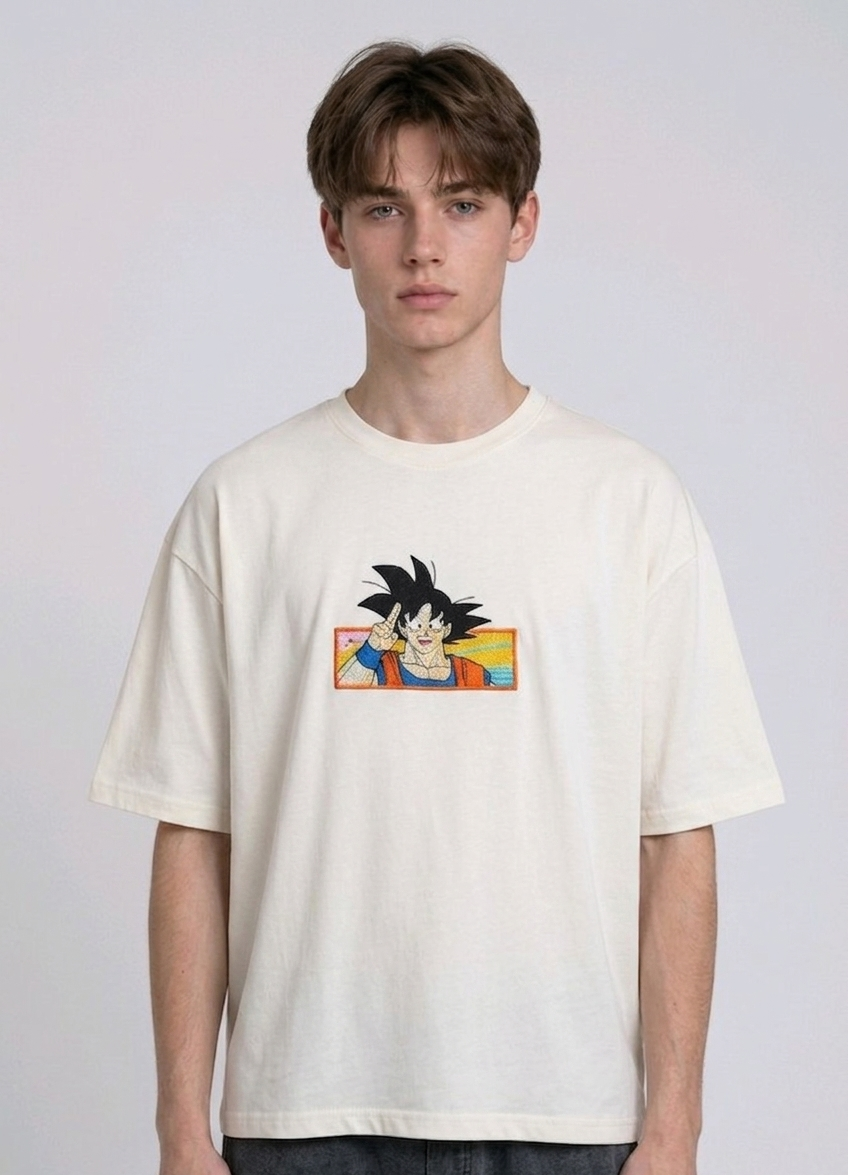 Front view of a male model with middle-parted brown hair wearing an Anetoonz dark grey mineral wash oversized t-shirt featuring a detailed, embroidered graphic of Son Goku from Dragon Ball Z giving a peace sign within a colorful framed background.
