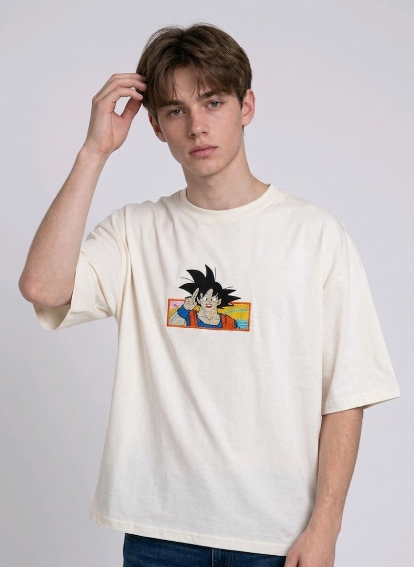 Front view of a male model with middle-parted brown hair wearing an Anetoonz dark grey mineral wash oversized t-shirt featuring a detailed, embroidered graphic of Son Goku from Dragon Ball Z giving a peace sign within a colorful framed background.